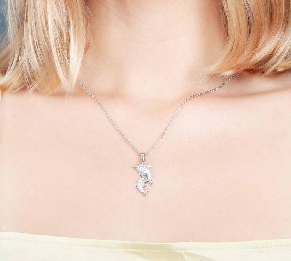 The picture shows a model wearing a 925 sterling silver, white gold vermeil, two dolphin pendant with topaz.