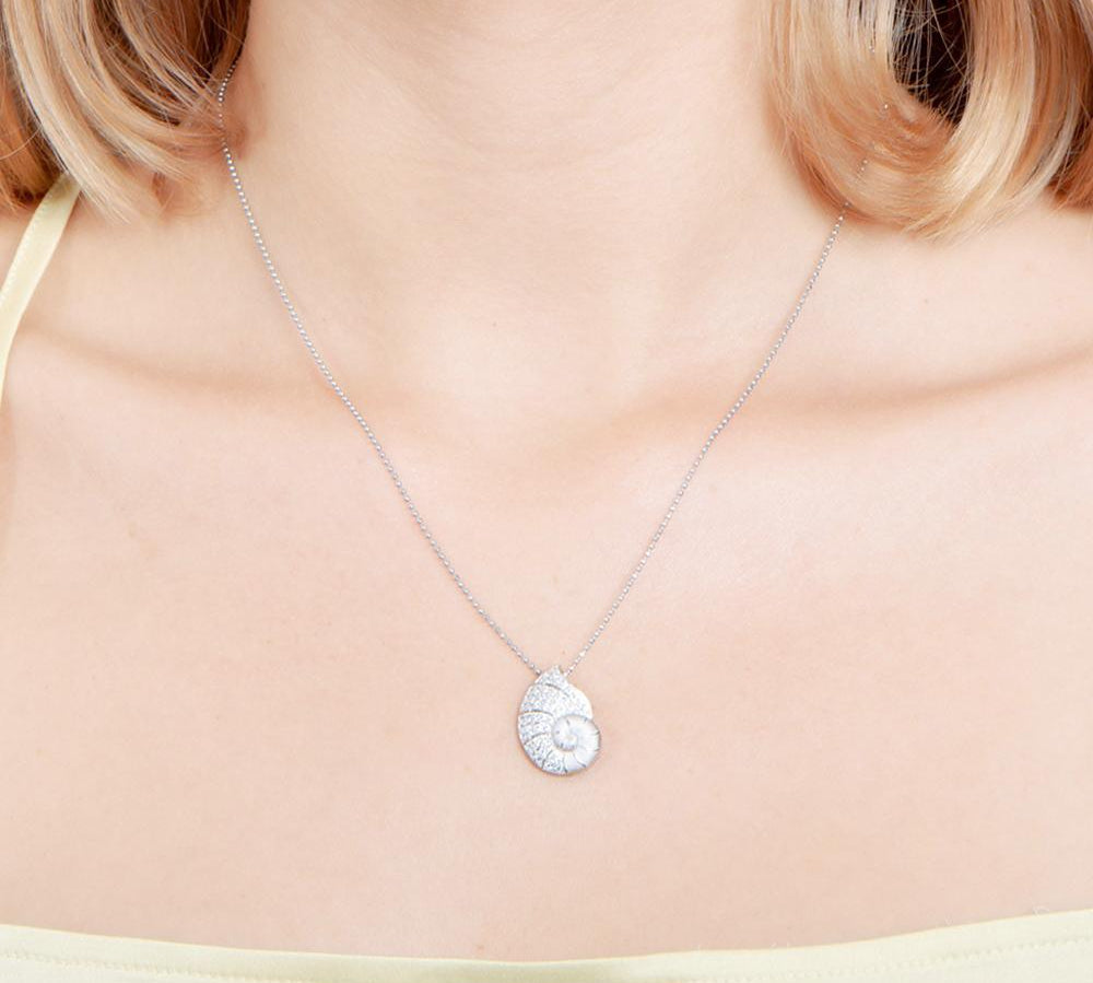 The picture shows a model wearing a 925 sterling silver, white gold vermeil, pavé nautilus pendant with topaz.