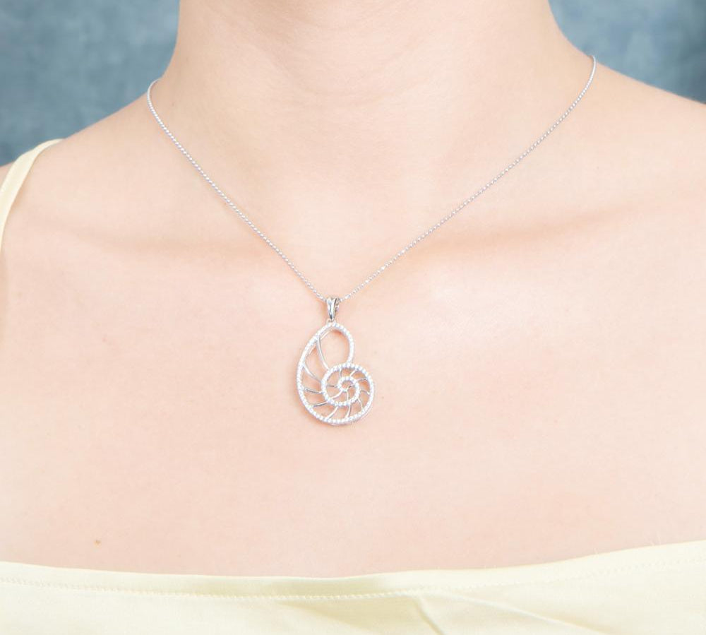 The picture shows a model wearing a 925 sterling silver pavé white gold vermeil nautilus shell pendant with topaz.