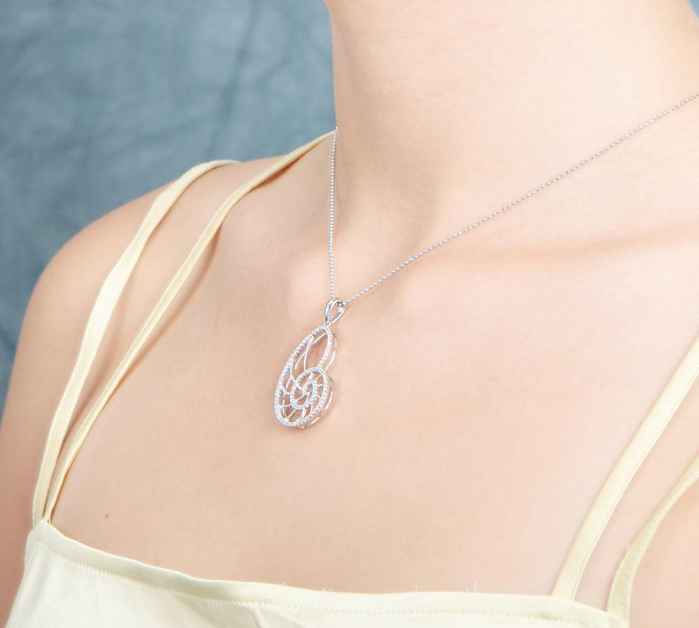 The picture shows a model wearing a 925 sterling silver pavé white gold vermeil nautilus shell pendant with topaz.