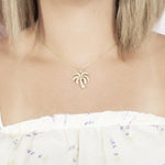 In this photo there is a model with blonde hair and a white shirt with flowers, wearing a yellow gold palm tree pendant with topaz gemstones.