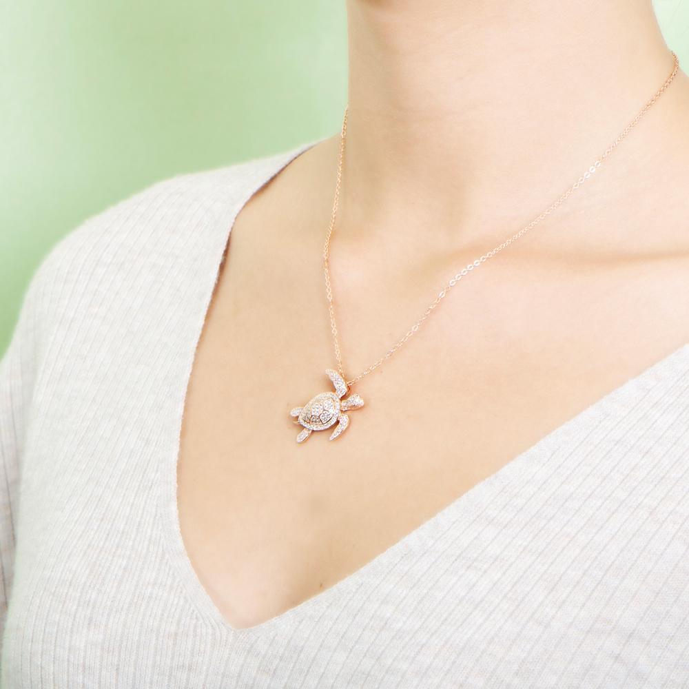 The picture shows a model wearing a 925 sterling silver rose gold vermeil sea turtle pendant with cubic zirconia.