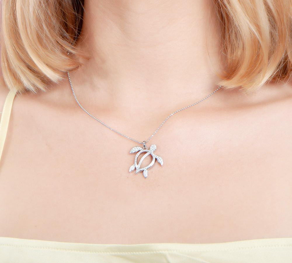 In this photo there is a model with blonde hair and a yellow shirt, wearing a white gold sea turtle pendant with topaz gemstones.