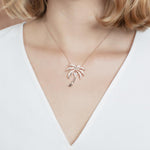 In this photo there is a model with blonde hair and a white shirt, wearing a rose gold palm tree pendant with topaz gemstones.