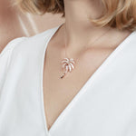 In this photo there is a model turned slightly to the left with blonde hair and a white shirt, wearing a rose gold palm tree pendant with topaz gemstones.