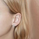 In this photo there is a close-up of a model with blonde hair wearing a pair of sterling silver palm tree stud earrings with topaz gemstones.
