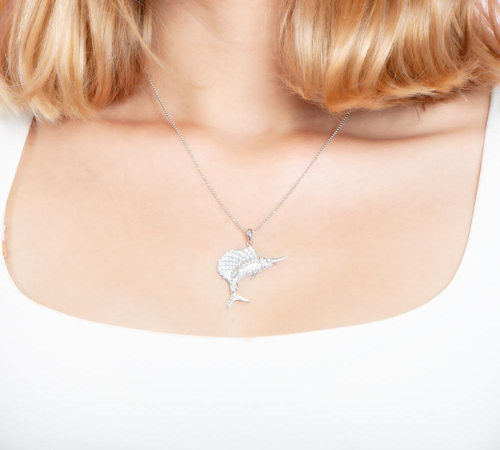 The picture shows a model wearing a 925 sterling silver, white gold vermeil, sailfish pendant with topaz.