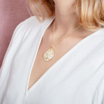 The picture shows a model wearing a large 925 sterling silver, yellow gold vermeil, pavé sand dollar pendant with topaz.