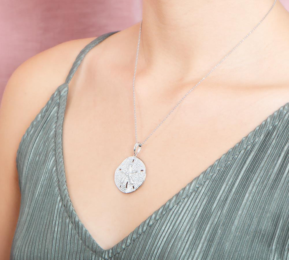 The picture shows a model wearing a large 925 sterling silver, white gold vermeil, pavé sand dollar pendant with topaz.