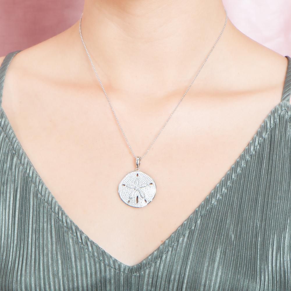 The picture shows a model wearing a large 925 sterling silver, white gold vermeil, pavé sand dollar pendant with topaz.