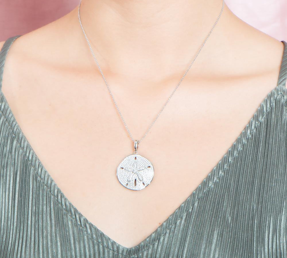 The picture shows a model wearing a large 925 sterling silver, white gold vermeil, pavé sand dollar pendant with topaz.