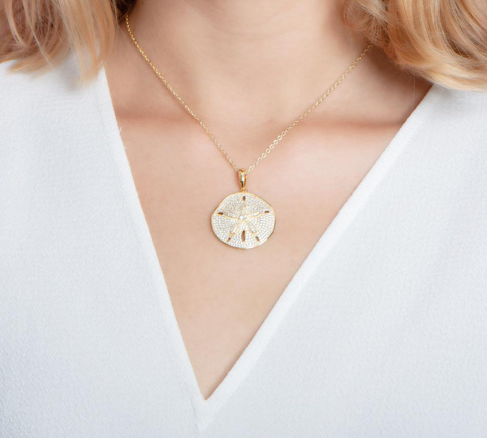 The picture shows a model wearing a large 925 sterling silver, yellow gold vermeil, pavé sand dollar pendant with topaz.