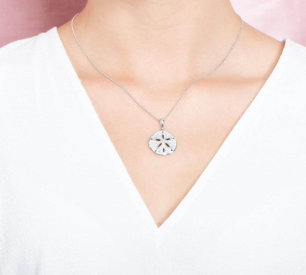 The picture shows a model wearing a medium 925 sterling silver, white gold vermeil, pavé sand dollar pendant with topaz.
