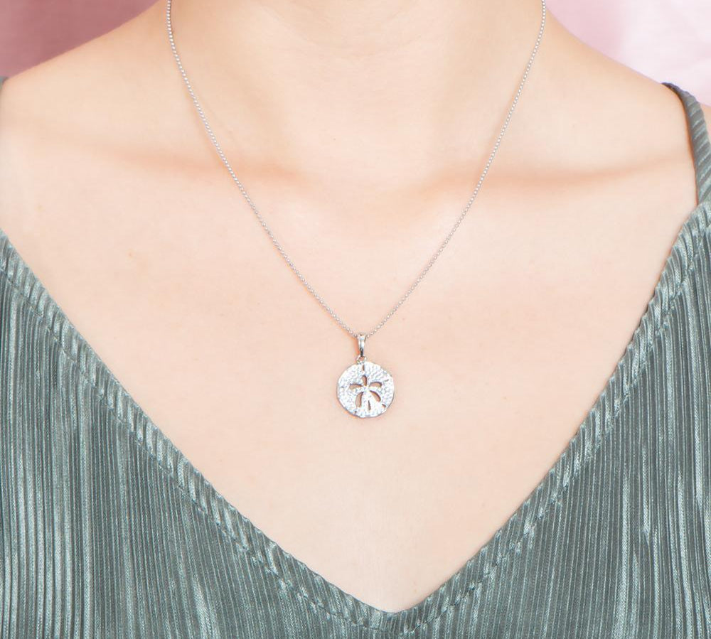 The picture shows a model wearing a small 925 sterling silver, white gold vermeil, pavé sand dollar pendant with topaz.