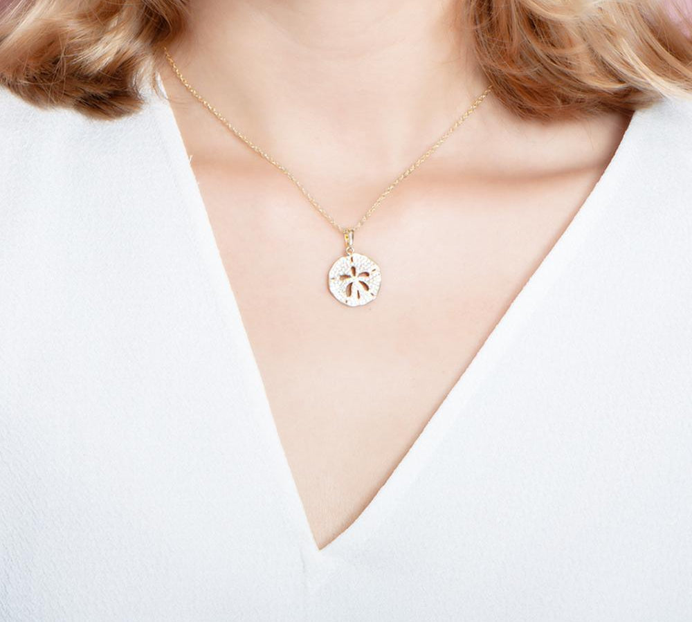 The picture shows a model wearing a small 925 sterling silver, yellow gold vermeil, pavé sand dollar pendant with topaz.