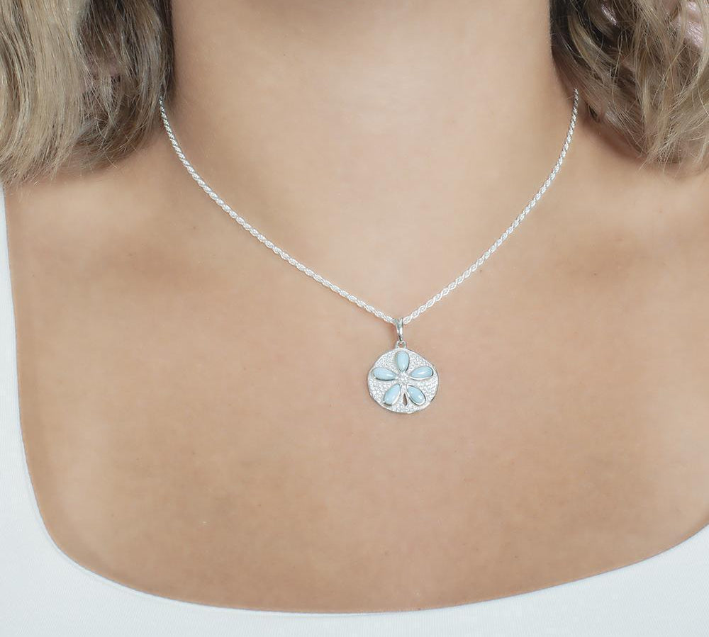 The picture shows a model wearing a 925 sterling silver pavé sand dollar pendant with larimar and topaz.