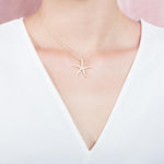 The picture shows a model wearing a 925 sterling silver, yellow gold vermeil, sea star pendant with topaz.