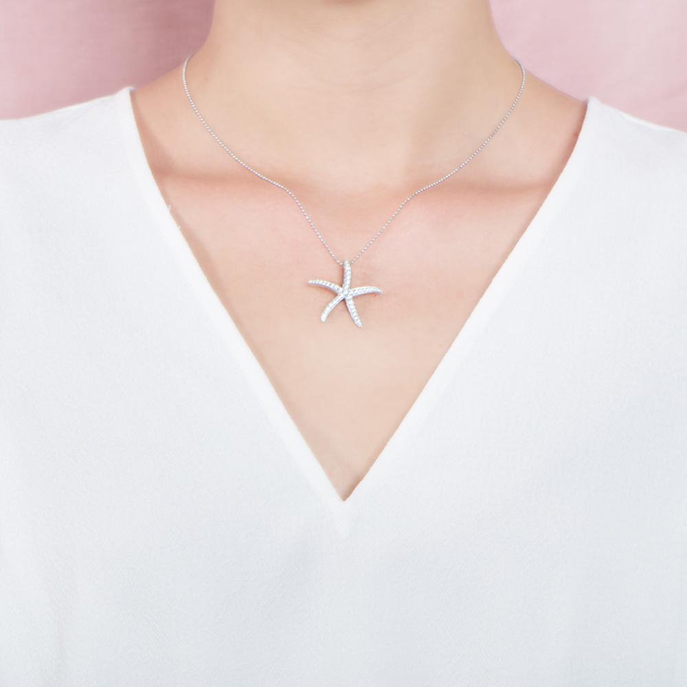 The picture shows a model wearing a 925 sterling silver, white gold vermeil, sea star pendant with topaz.