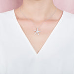 The picture shows a model wearing a 925 sterling silver, white gold vermeil, sea star pendant with topaz.