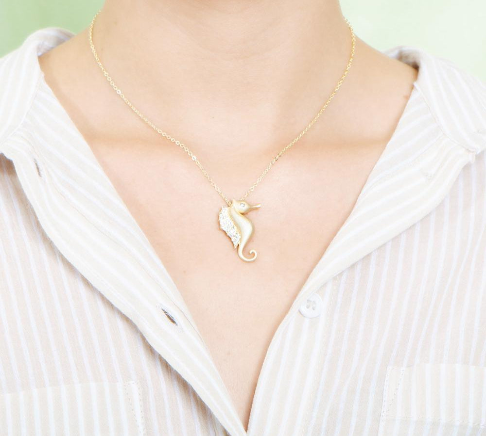 The picture shows a model wearing a 925 sterling silver, yellow gold vermeil, pavé seahorse pendant with topaz.