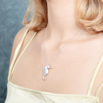 The picture shows a model wearing a 925 sterling silver, white gold vermeil, pavé seahorse pendant with topaz.