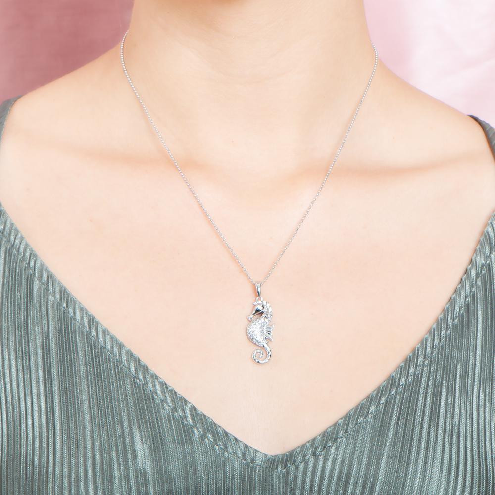 The picture shows a model wearing a 925 sterling silver, white gold vermeil, pavé seahorse pendant with topaz.