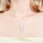 The picture shows a model wearing a 925 sterling silver, white gold vermeil, pavé seahorse pendant with topaz.