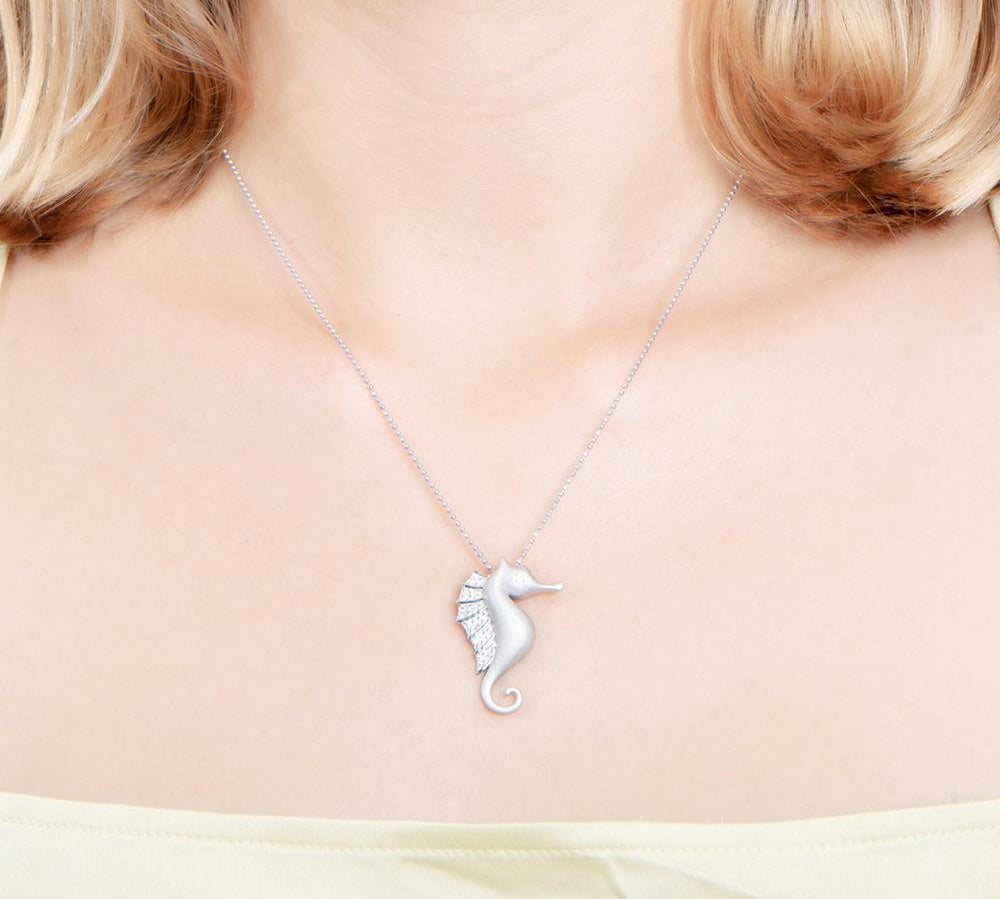 The picture shows a model wearing a 925 sterling silver, white gold vermeil, pavé seahorse pendant with topaz.
