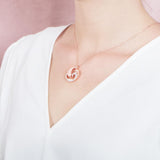The picture shows a model wearing a 925 sterling silver, rose gold vermeil, dolphin and wave pendant with topaz.