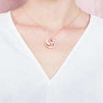 The picture shows a model wearing a 925 sterling silver, rose gold vermeil, dolphin and wave pendant with topaz.