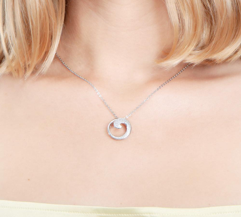 The photo is shows a model wearing a sterling silver pavé wave pendant with topaz.