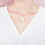 The picture shows a model wearing a 925 sterling silver, yellow gold vermeil, pavé whale tail medallion pendant with topaz.
