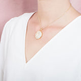 The picture shows a model wearing a 925 sterling silver, yellow gold vermeil, pavé whale tail medallion pendant with topaz.