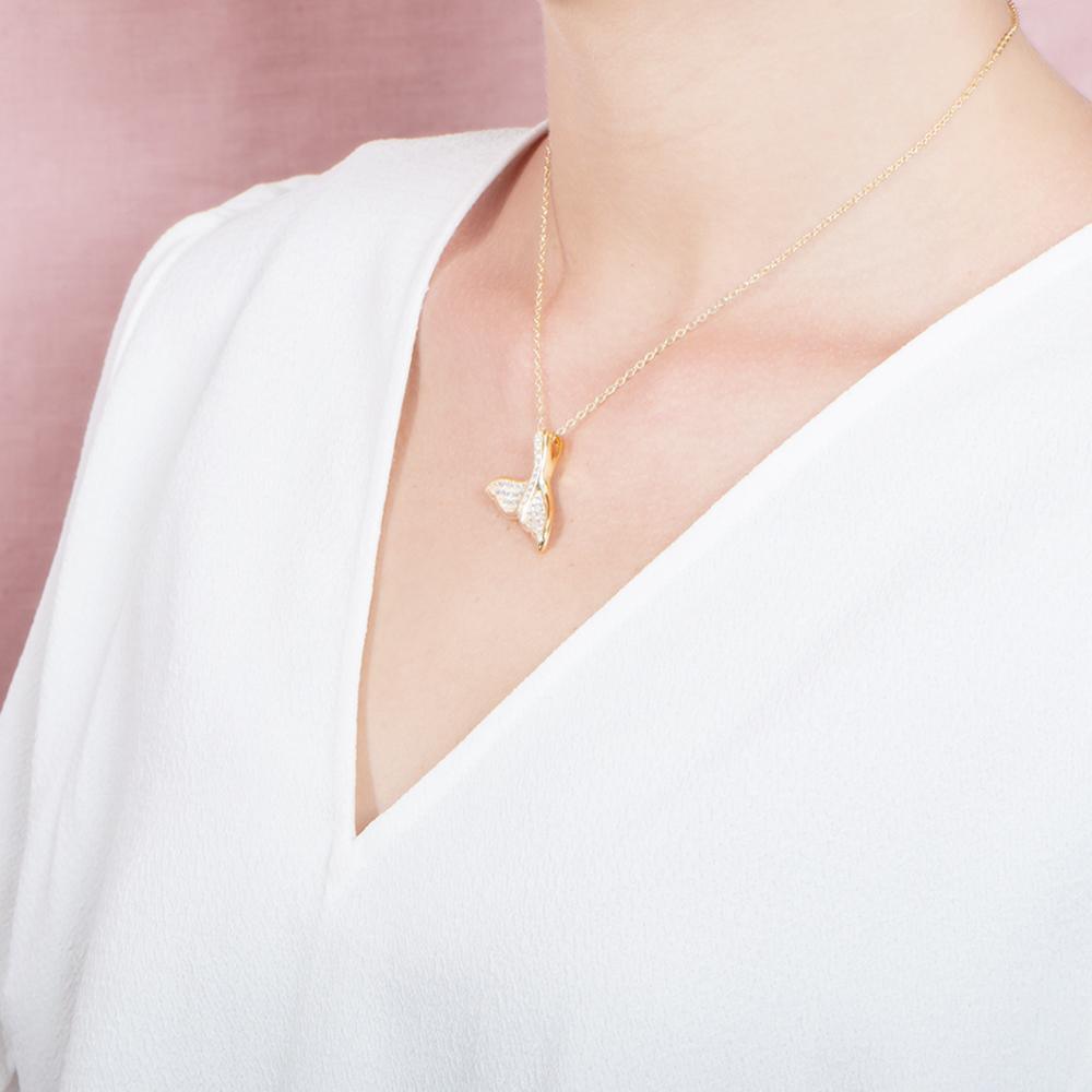 The picture shows a model wearing a 925 sterling silver, yellow gold vermeil, pavé whale tail pendant with topaz.