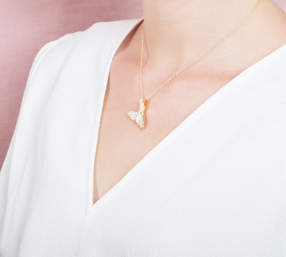 The picture shows a model wearing a 925 sterling silver, yellow gold vermeil, pavé whale tail pendant with topaz.