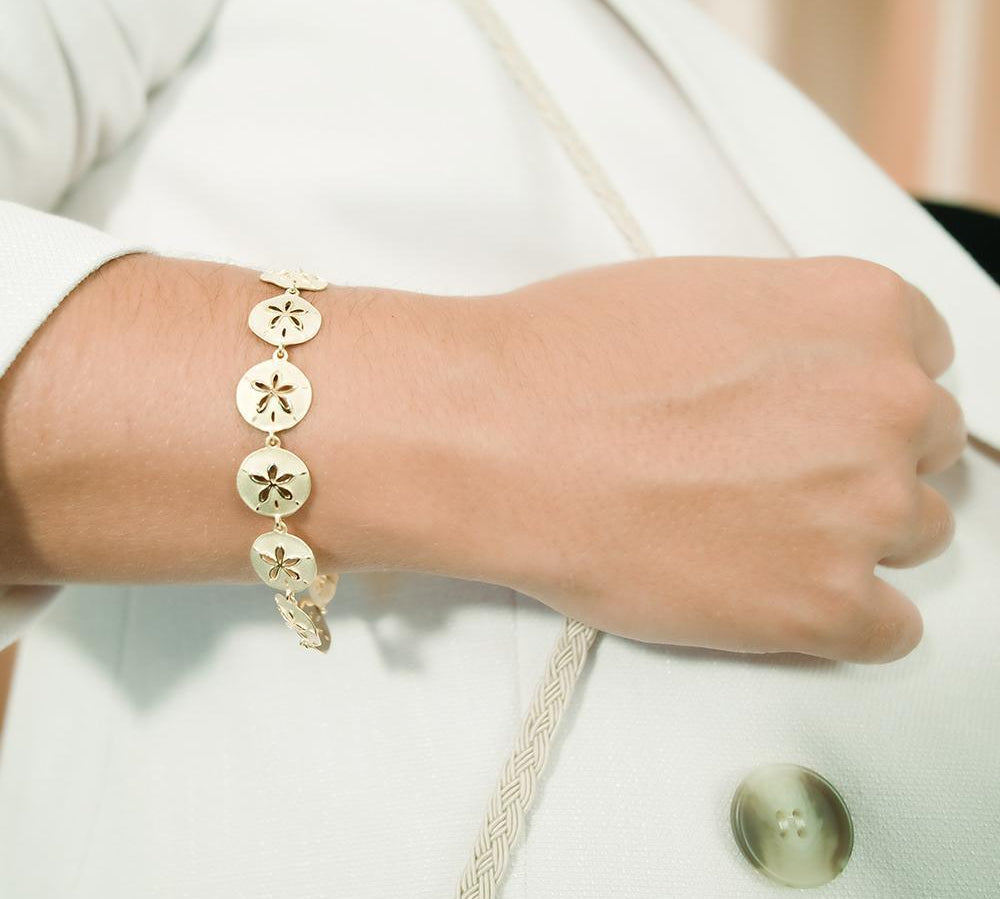 The picture shows a model wearing a yellow gold sand dollar bracelet.