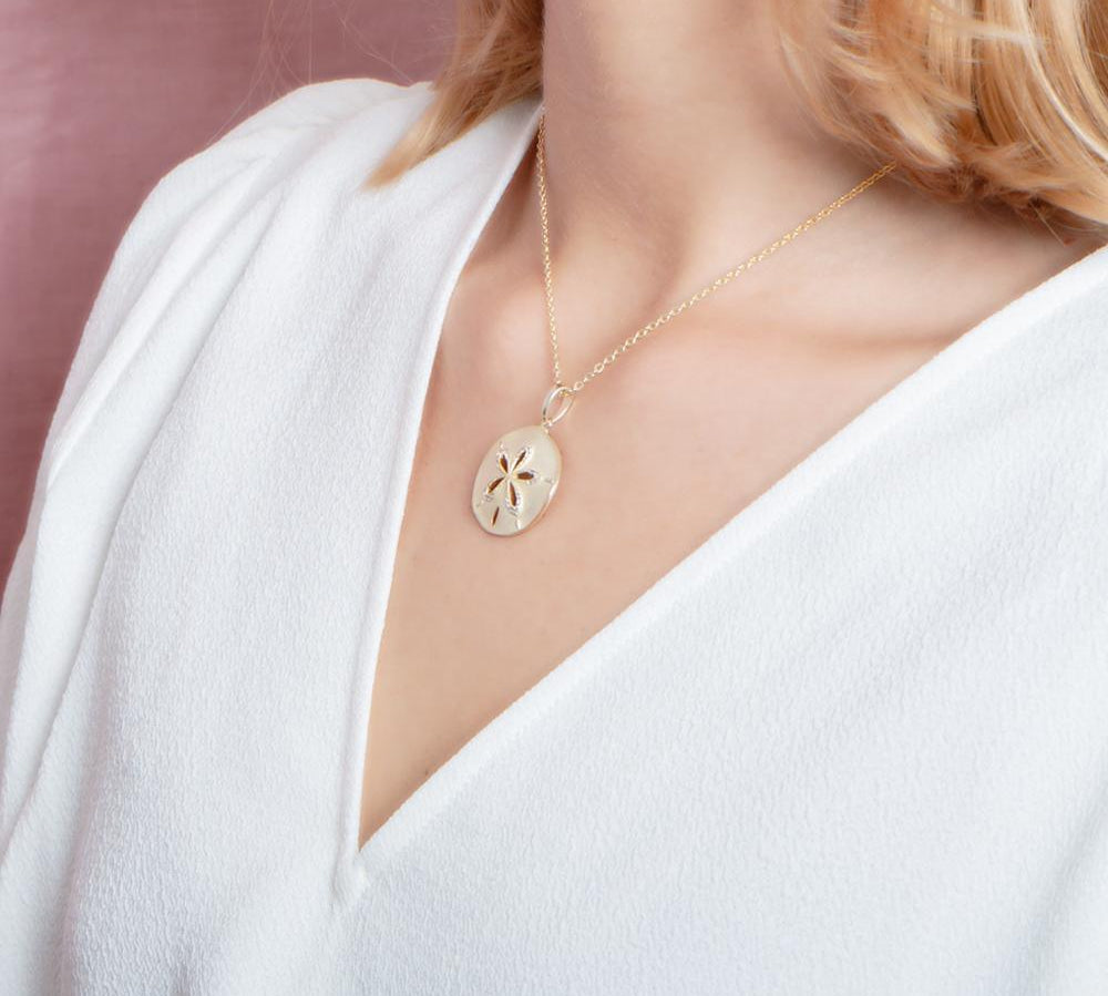 The picture shows a model wearing a yellow gold sand dollar cut out pendant.
