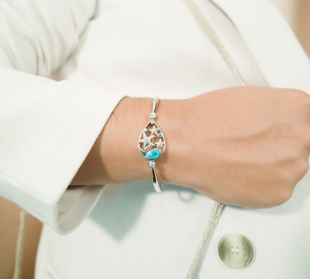 The picture shows a model wearing a 925 sterling silver bracelet with three starfish, seaweed, and topaz, aquamarine, and larimar gemstones.