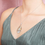 The picture shows a model wearing a two-tone white and yellow gold sea horse mandorla pendant with aquamarine and topaz.