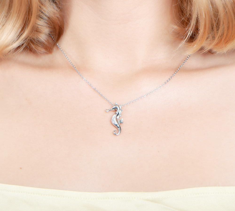 In this photo there is a model with blonde hair and a yellow shirt wearing a sterling silver seahorse pendant with topaz.