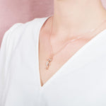In this photo there is a model turned to the left with a white shirt, wearing a rose gold seahorse pendant with topaz gemstones.