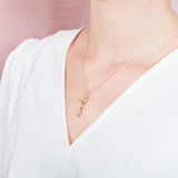 In this photo there is a model turned to the left with a white shirt, wearing a rose gold seahorse pendant with topaz gemstones.