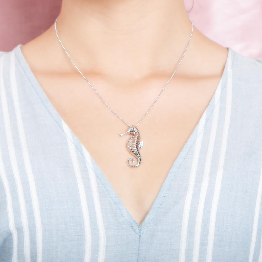 In this photo there is a model with a light blue and white striped shirt, wearing a sterling silver seahorse pendant.