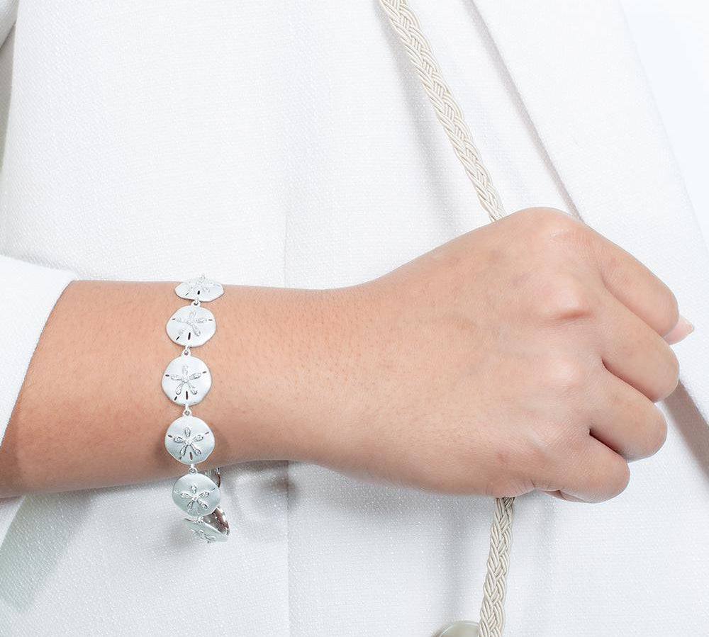 The picture shows a model wearing a white gold sand dollar bracelet with topaz.