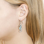 The picture shows a model wearing a 925 sterling silver larimar seahorse hook earring with topaz.