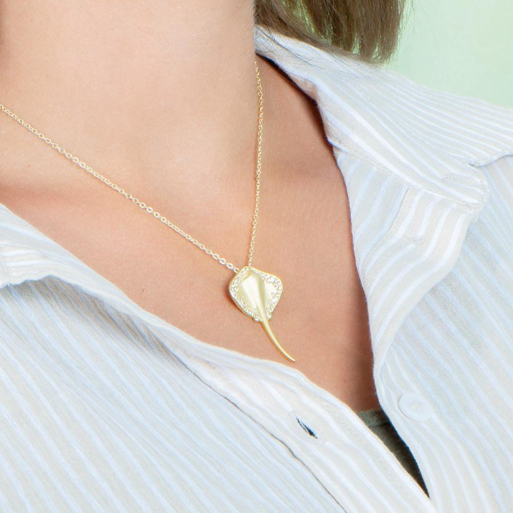The picture shows a model wearing a yellow gold manta ray pendant with topaz.