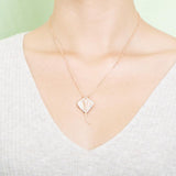 The picture shows a model wearing a rose gold manta ray pendant with topaz.