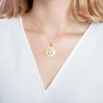 The picture shows a model wearing a yellow gold sand dollar pendant with topaz.