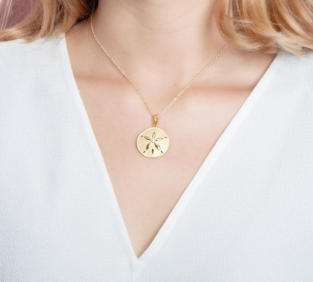 The picture shows a model wearing a yellow gold sand dollar pendant with topaz.