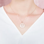 The picture shows a model wearing a rose gold sand dollar pendant with topaz.